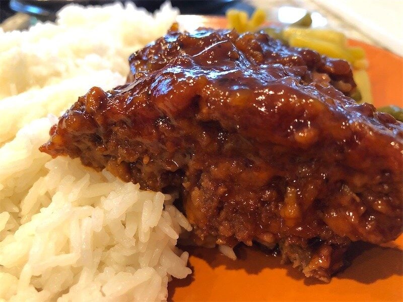 A slice of delicious homemade meatloaf served on a plate with jasmine rice and green beans and yellow beans