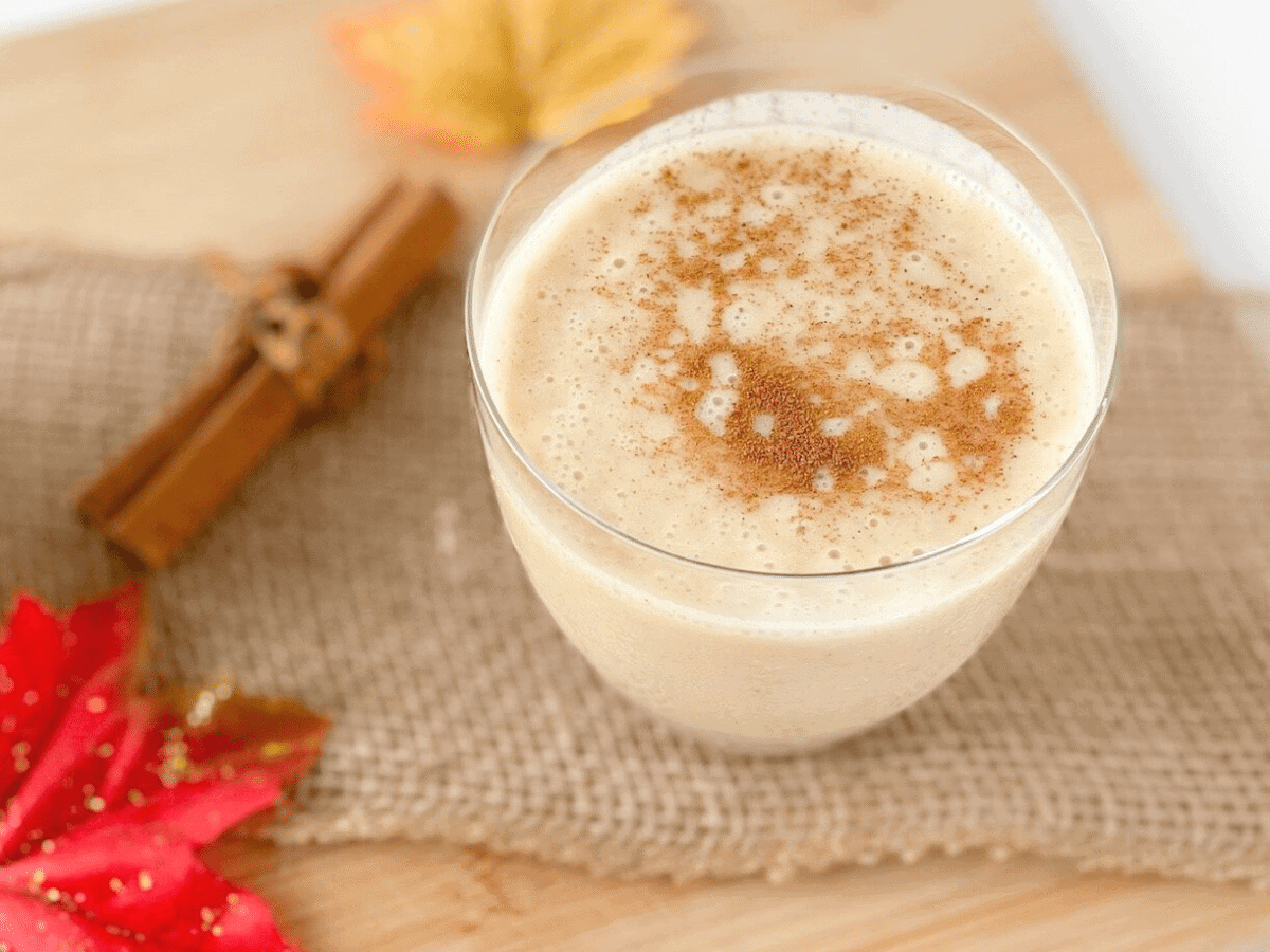 Closeup of a pumpkin pie smoothie with a sprinkle of cinnamon on top, with cinnamon sticks beside the glass