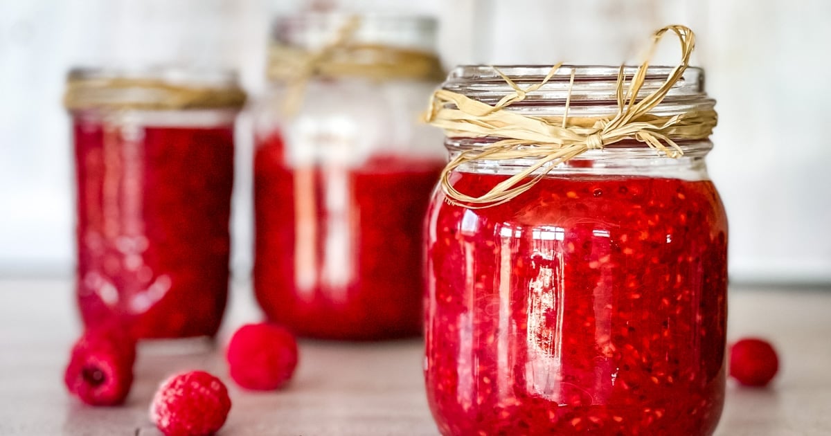 Red raspberry jam in glass jars cooling on a counter.