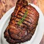 Smoked prime rib roast on white serving platter, with a sprig of rosemary on top.
