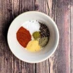 The smoked paprika, kosher salt, cracked black pepper, garlic powder, rosemary, and thyme in a white bowl, not mixed.