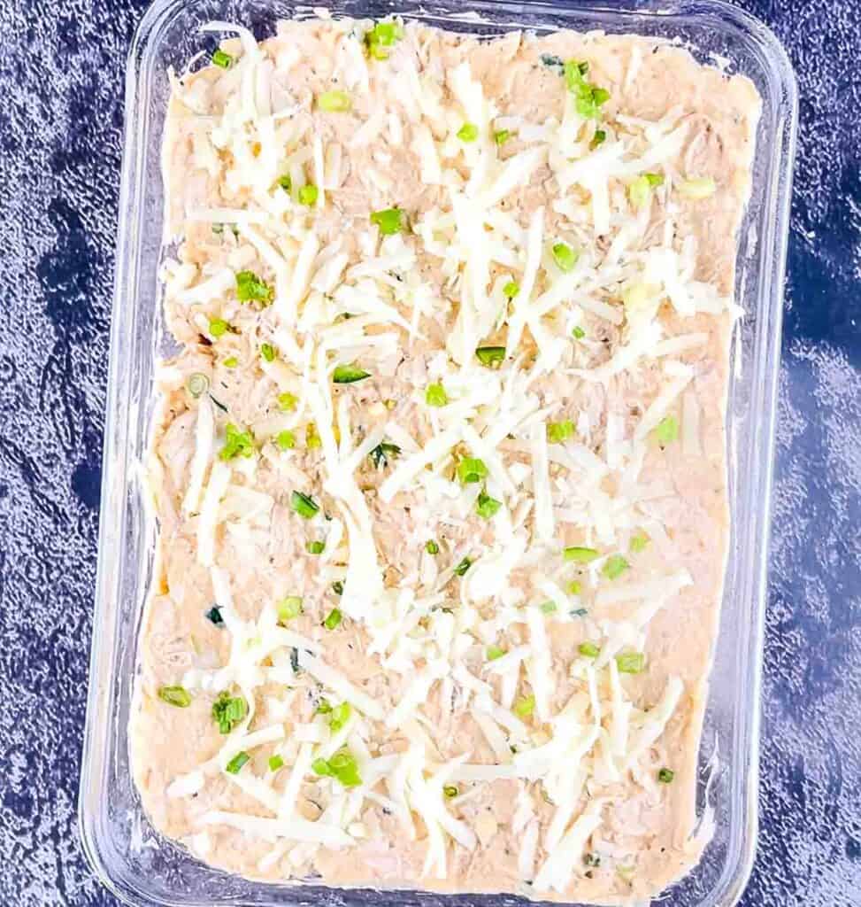 The buffalo chicken dip topped with extra shredded cheese and diced green onion in a glass casserole dish.