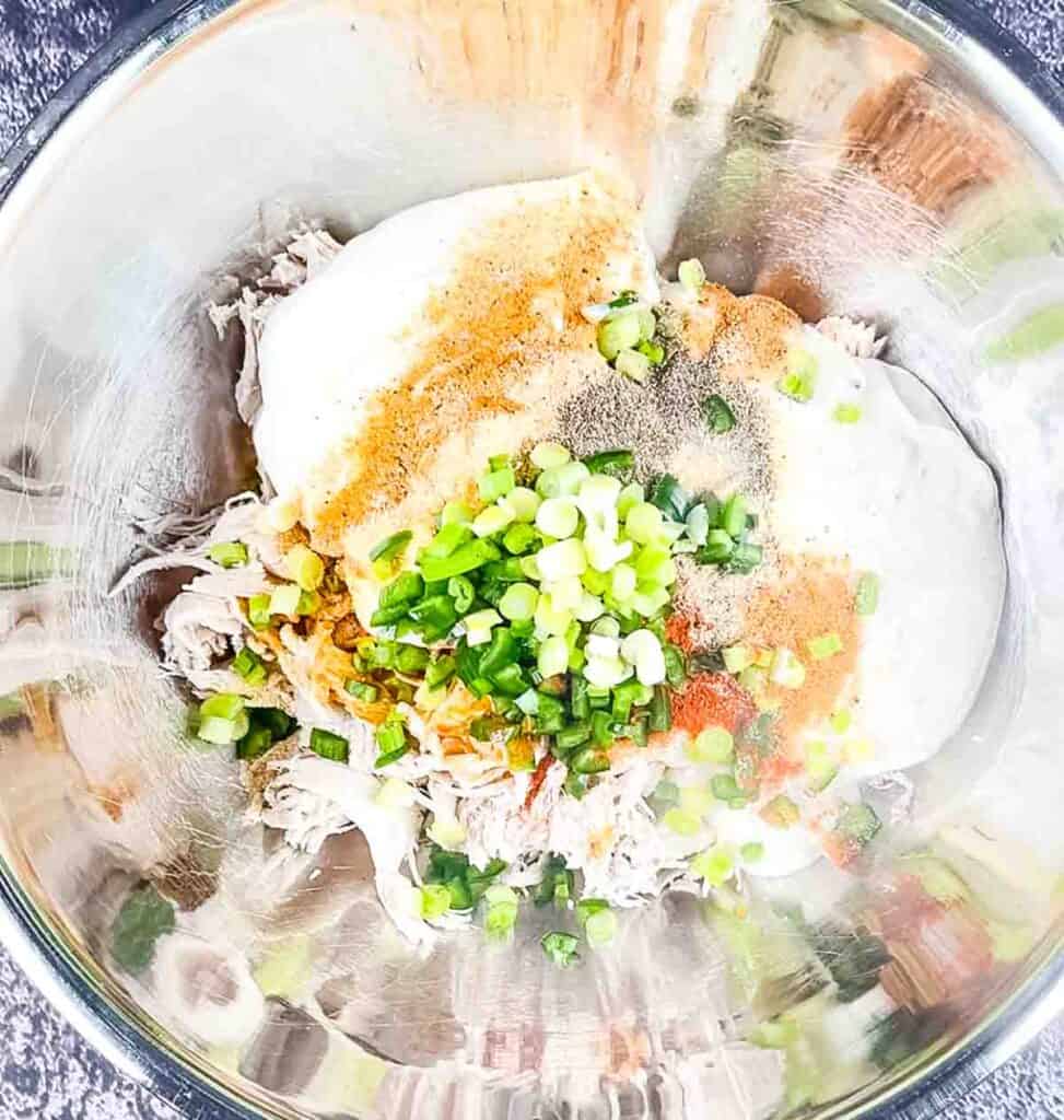 The shredded chicken in a bowl with sour cream, seasoning, hot sauce, and ranch dressing.