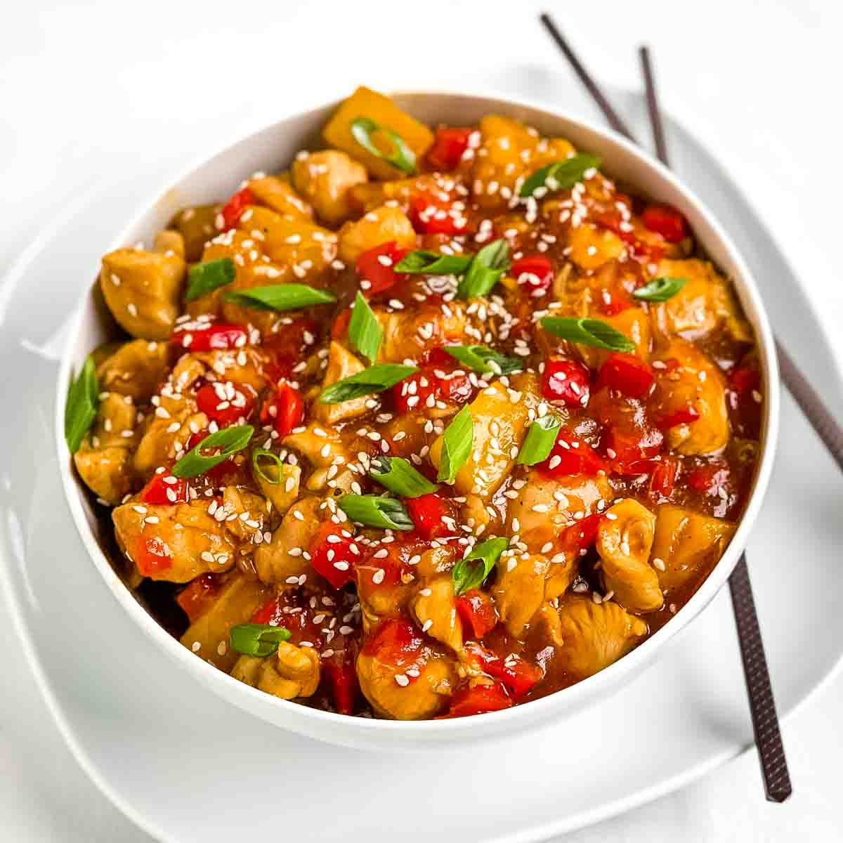 A white serving bowl filled with sauce pineapple chicken stir fry with colorful red bell pepper.