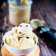 Ninja Creami coffee ice cream scoops in a white bowl, sprinkled with coffee beans and the pint jar and ice cream scoop in the background.