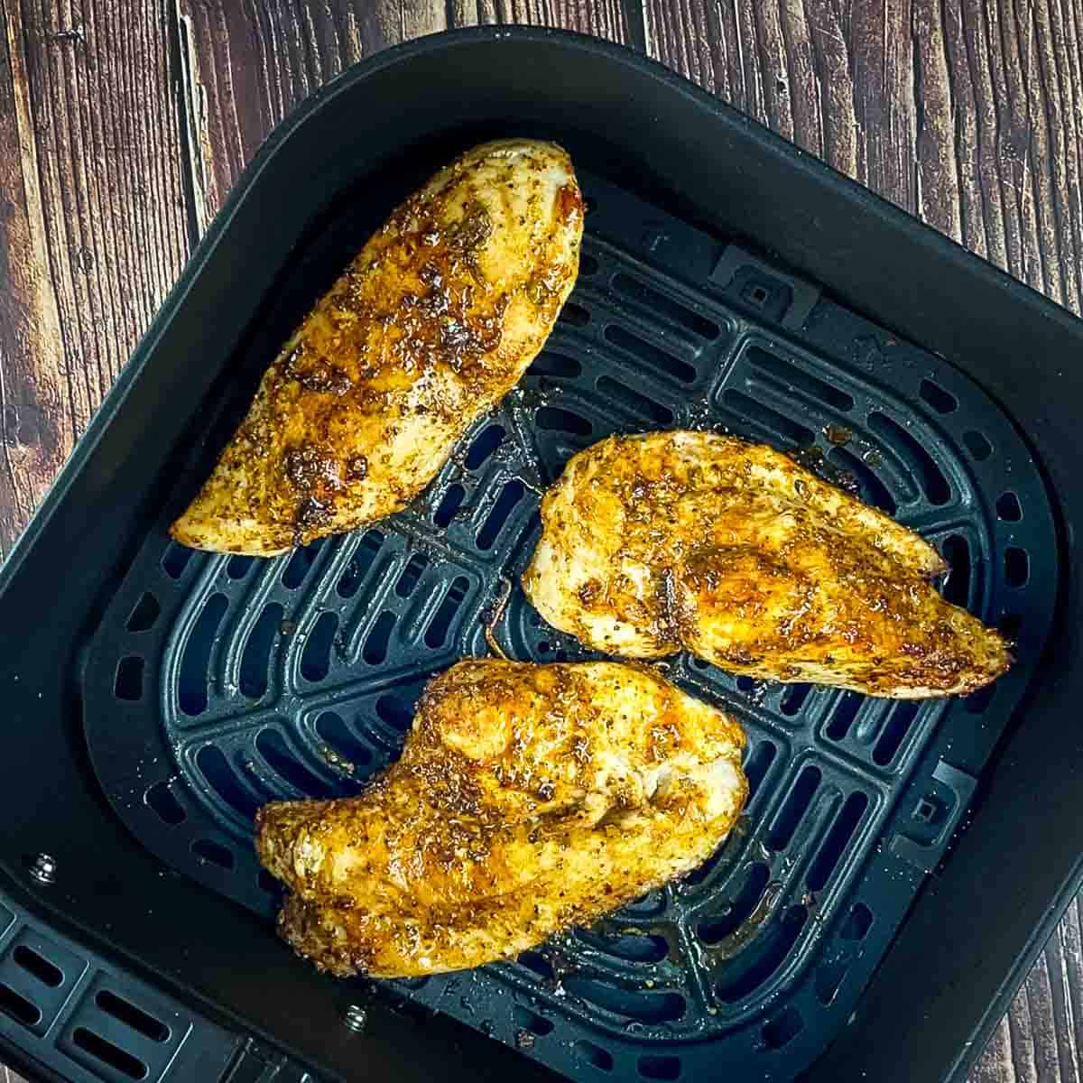 Three air fried thin chicken breasts resting in the air fryer basket.