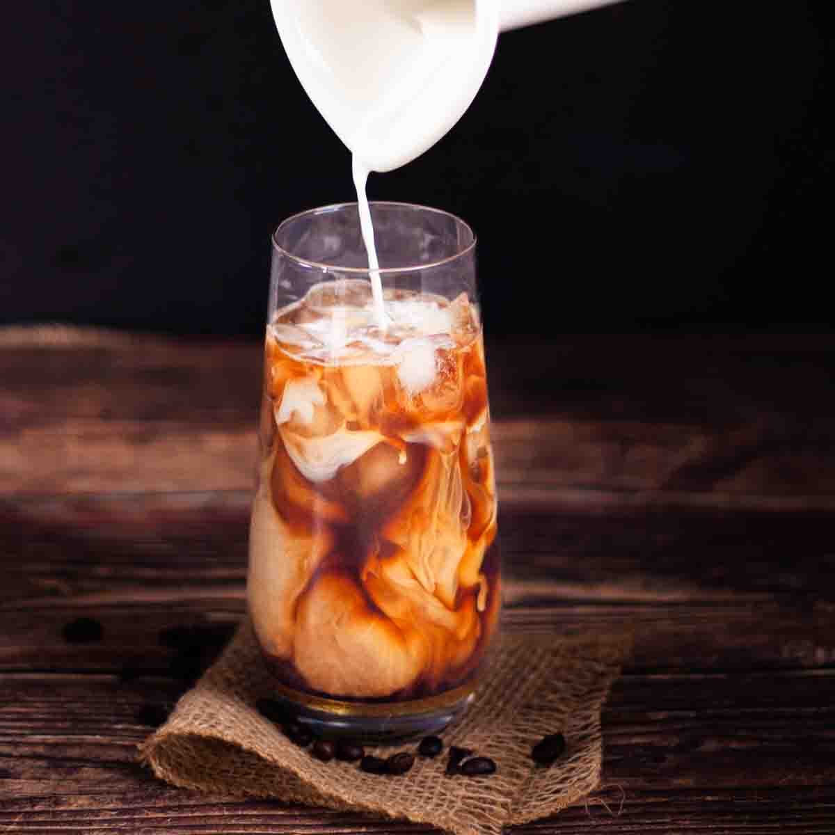 Half and half being poured into the glass filled with ice, coffee, and vanilla simple syrup.