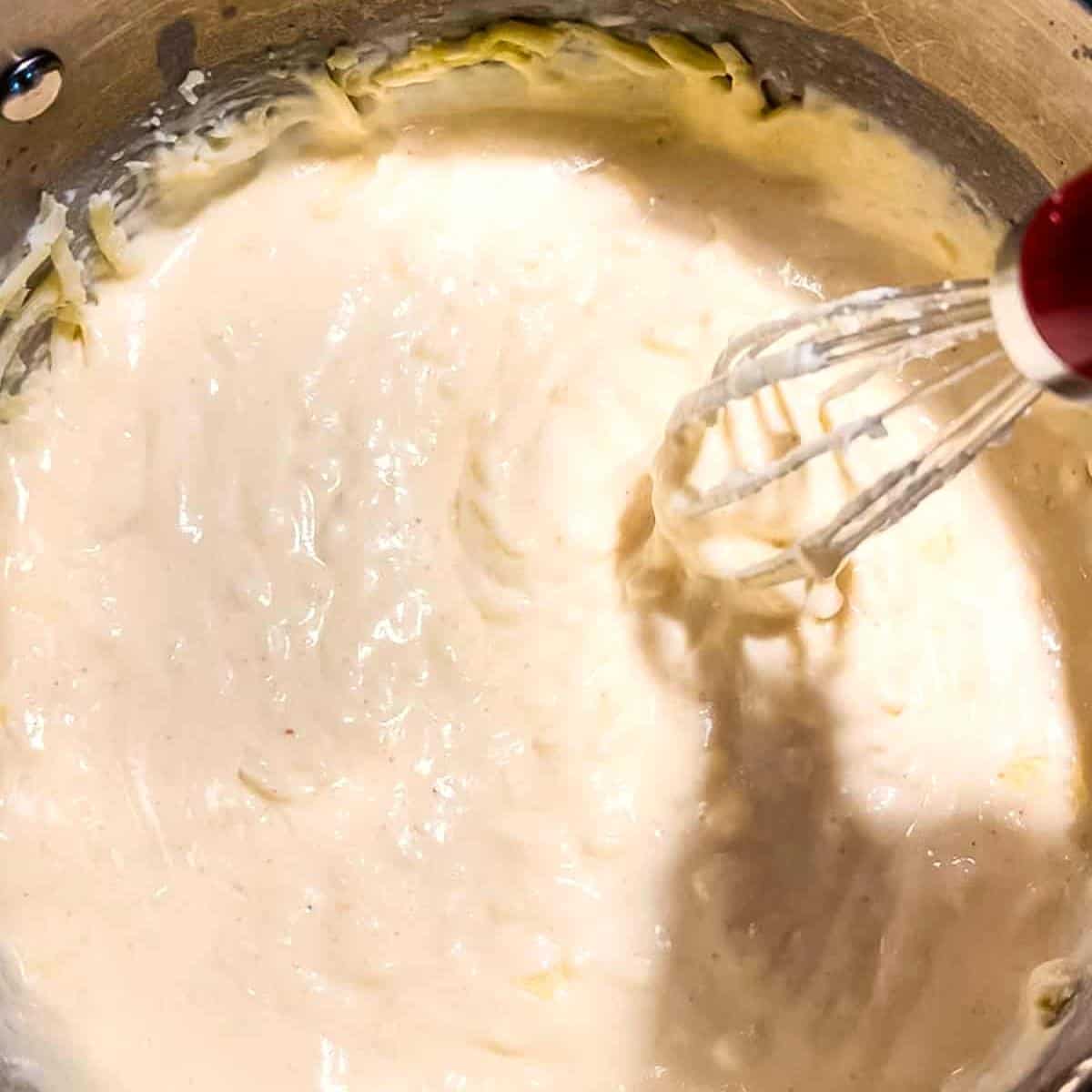 A whisk mixing the shredded cheese until it melts.