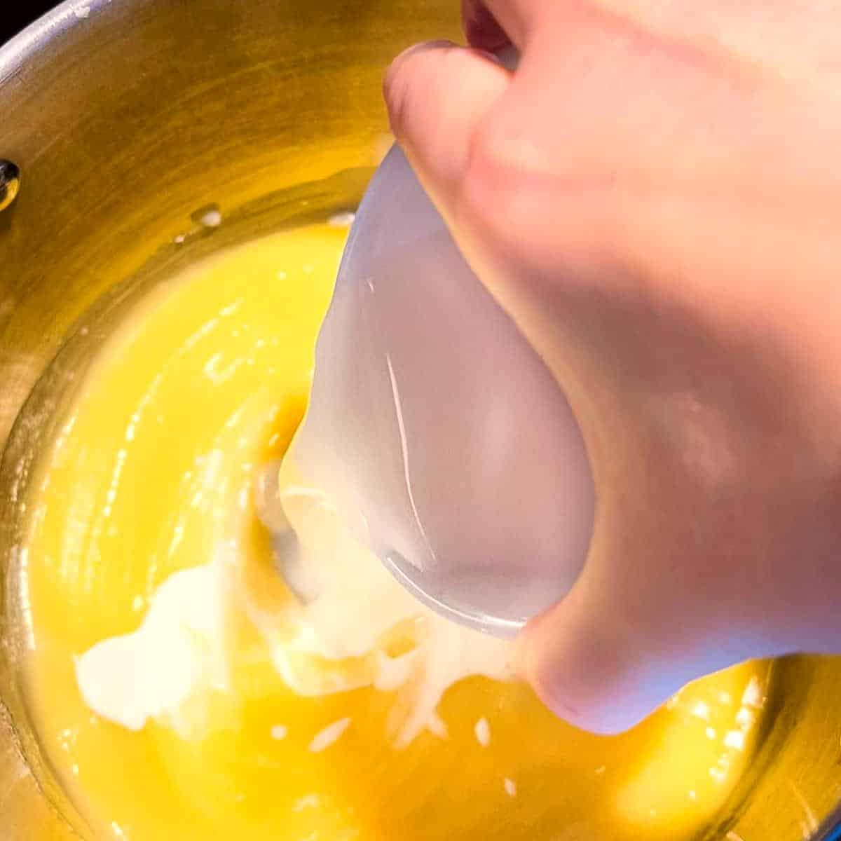 Milk being poured into a pot of sauce for the macaroni.