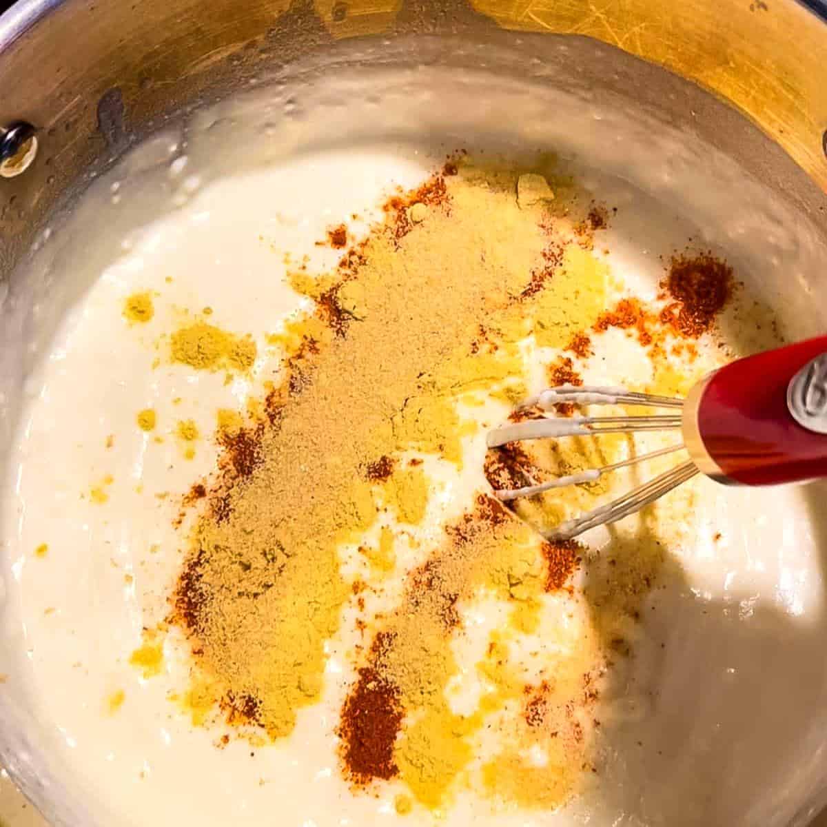 A whisk mixing the cream cheese and spices in the saucepan.