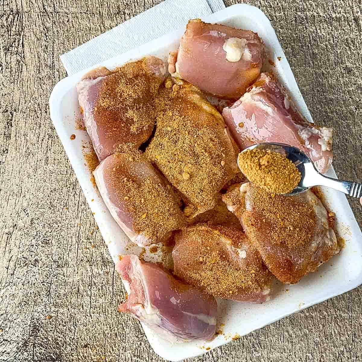 Generously coating chicken thighs with a red homemade dry rub of paprika, garlic powder, and brown sugar.