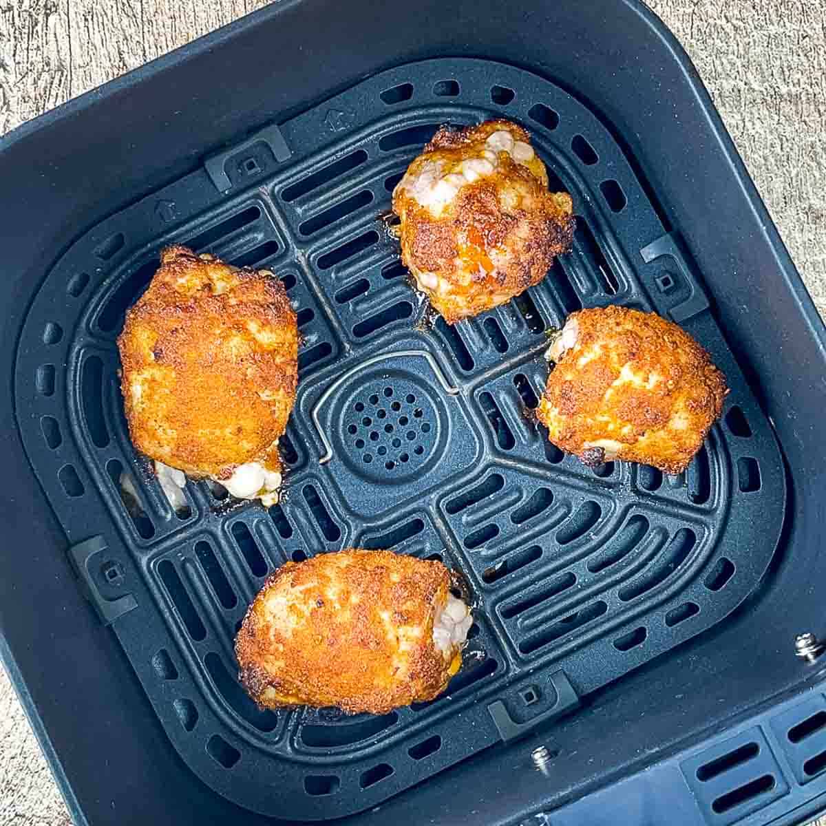 Flipping partially cooked golden brown chicken thighs in the air fryer basket.s.