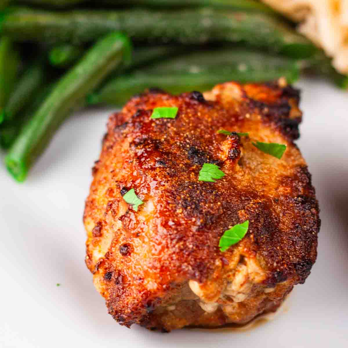 A juicy chicken thigh on a white plate showing a crispy mahogany colored exterior.