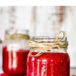 Jars of raspberry rhubarb jam on a table, with a scoop of it on a small spoon.