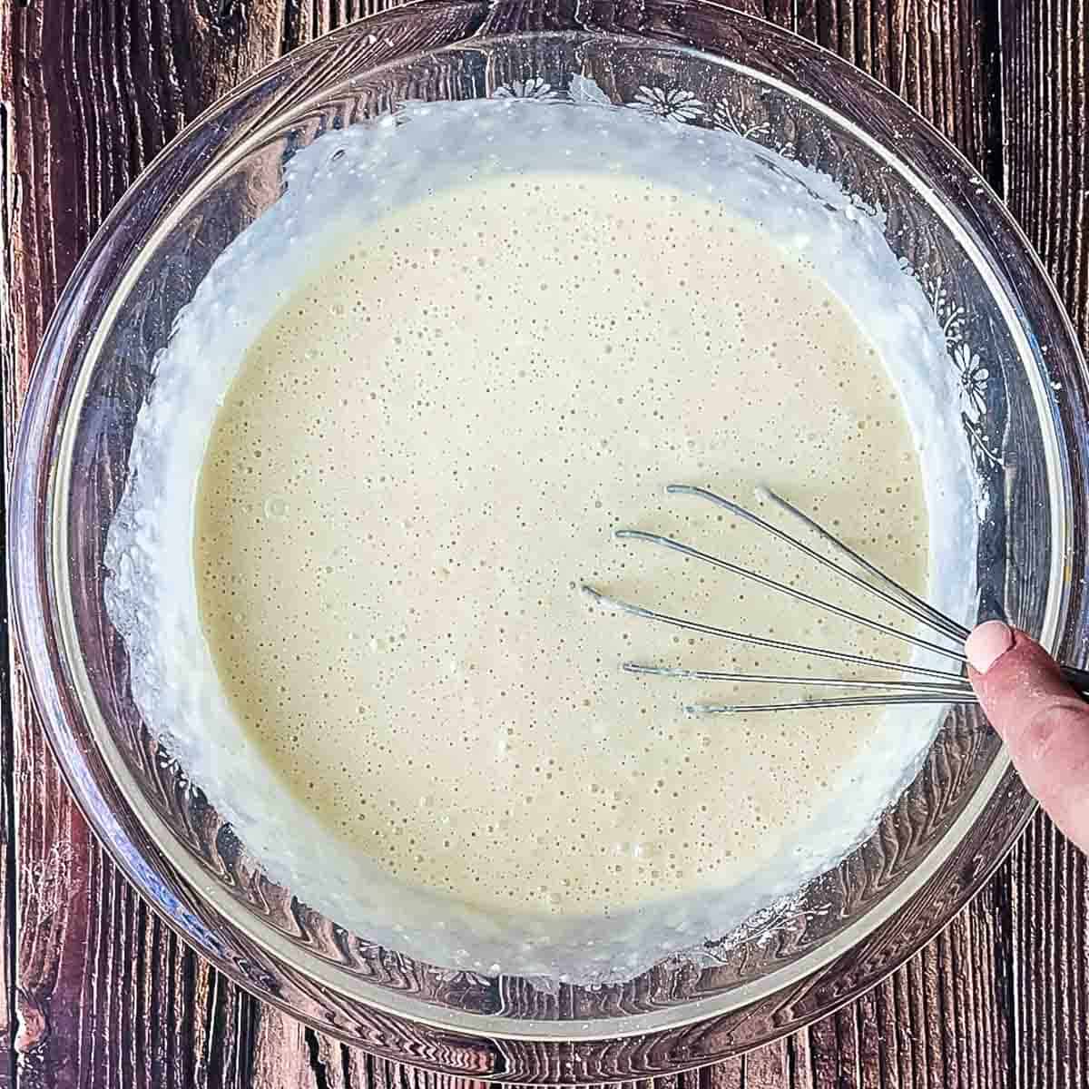A hand using a whisk to combine the sheet pan pancake ingredients.