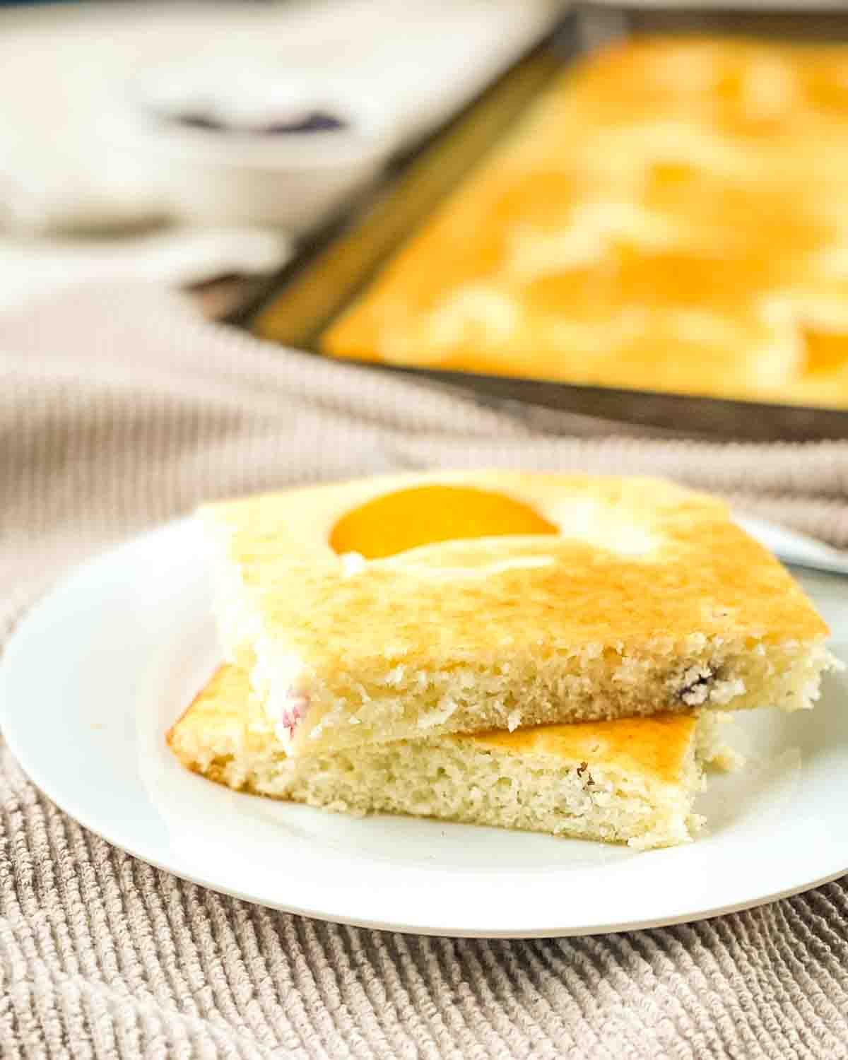 A stack of fluffy sheet pan pancakes with peaches and blueberries on a white plate.