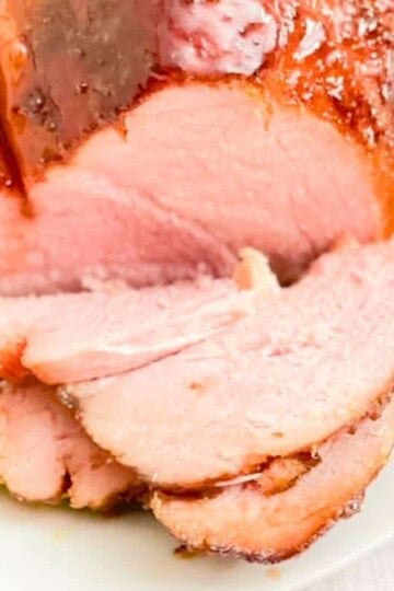 A glazed double smoked ham on a serving platter, sliced into thin slices.
