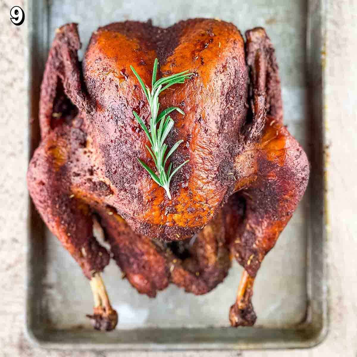 A whole smoked turkey on a baking sheet resting, garnished with fresh rosemary.