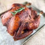 A smoked whole turkey on a baking sheet, perfectly browned and ready to eat, garnished with sprigs of fresh rosemary for added aroma and presentation.