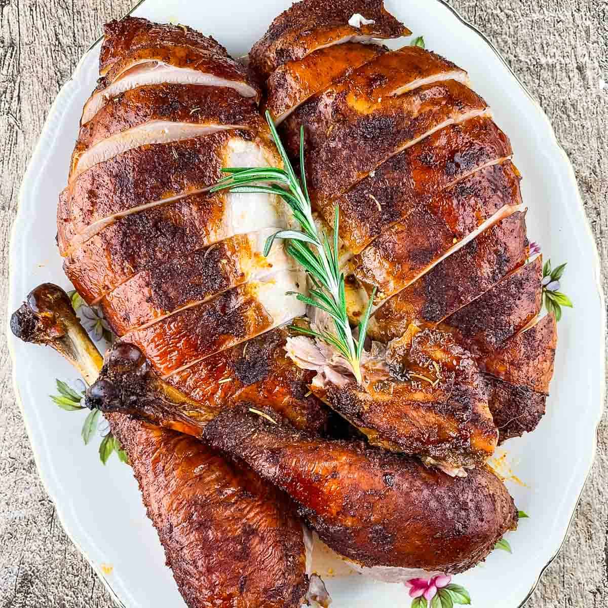 A serving platter of juicy smoked turkey, ready for serving, garnished with a sprig of fresh rosemary.