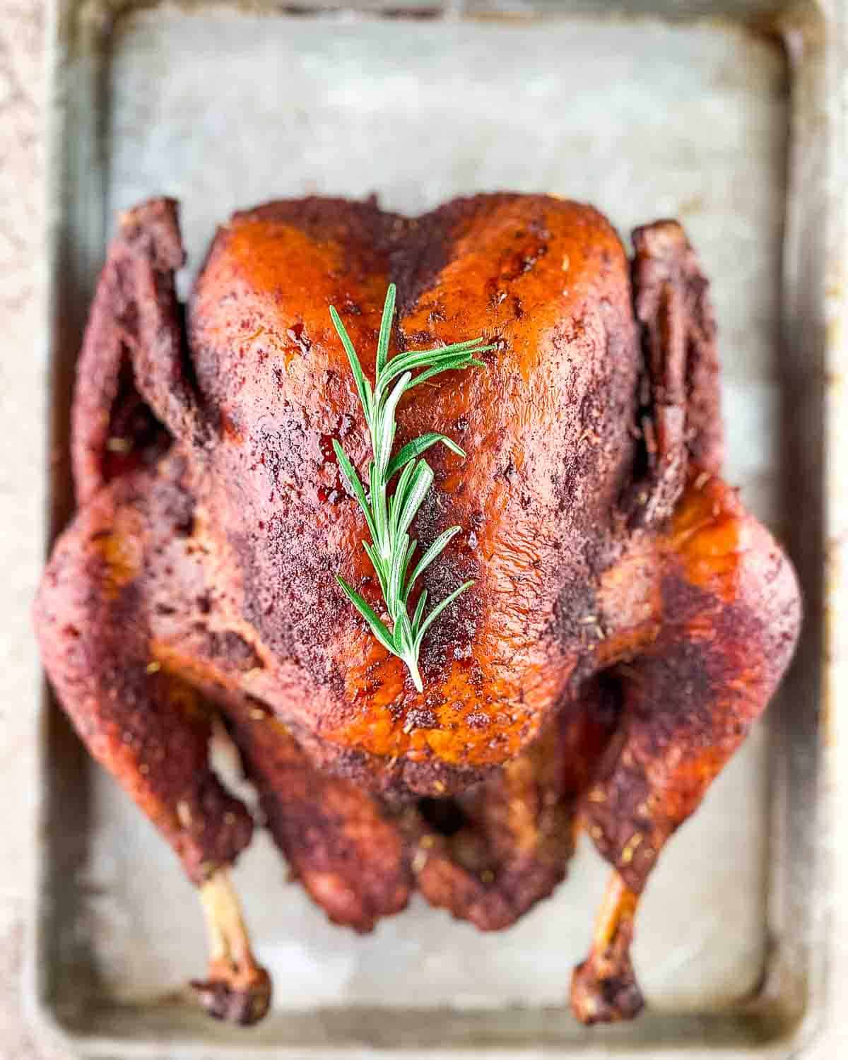 A juicy smoked whole turkey on a baking sheet, ready for carving.