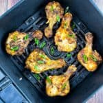 Golden brown and crispy butterflied chicken legs in the air fryer basket, garnished with chopped green onion.