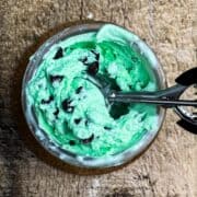 A Ninja Creami pint jar filled with mint chocolate ice cream and an ice cream scoop ready to scoop up some ice cream.
