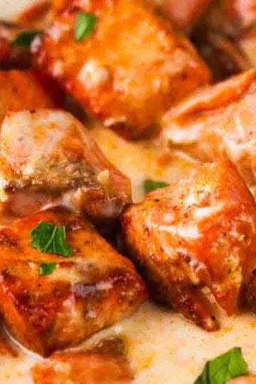 Salmon bites in a rich garlic cream sauce, served on a plate with fresh herbs.