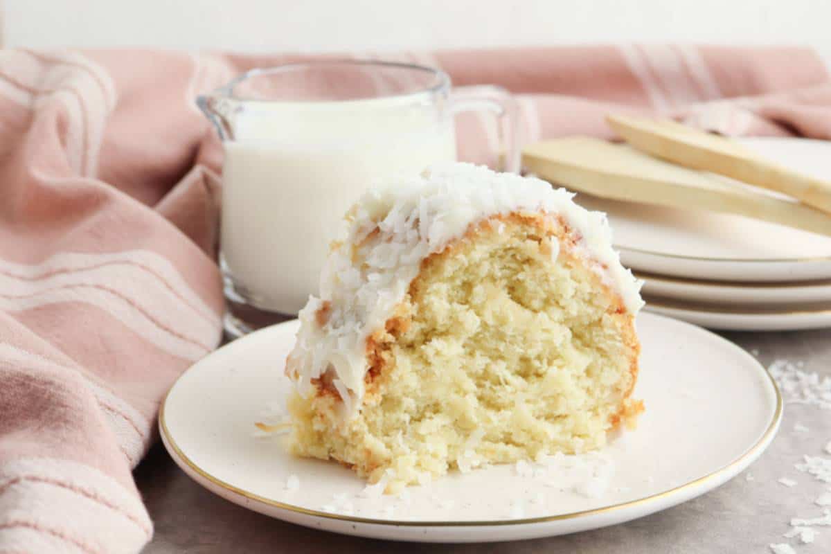 A slice of Coconut Cream Bundt Cake on a dessert plate, covered in smooth cream cheese frosting and sprinkled with shredded coconut.