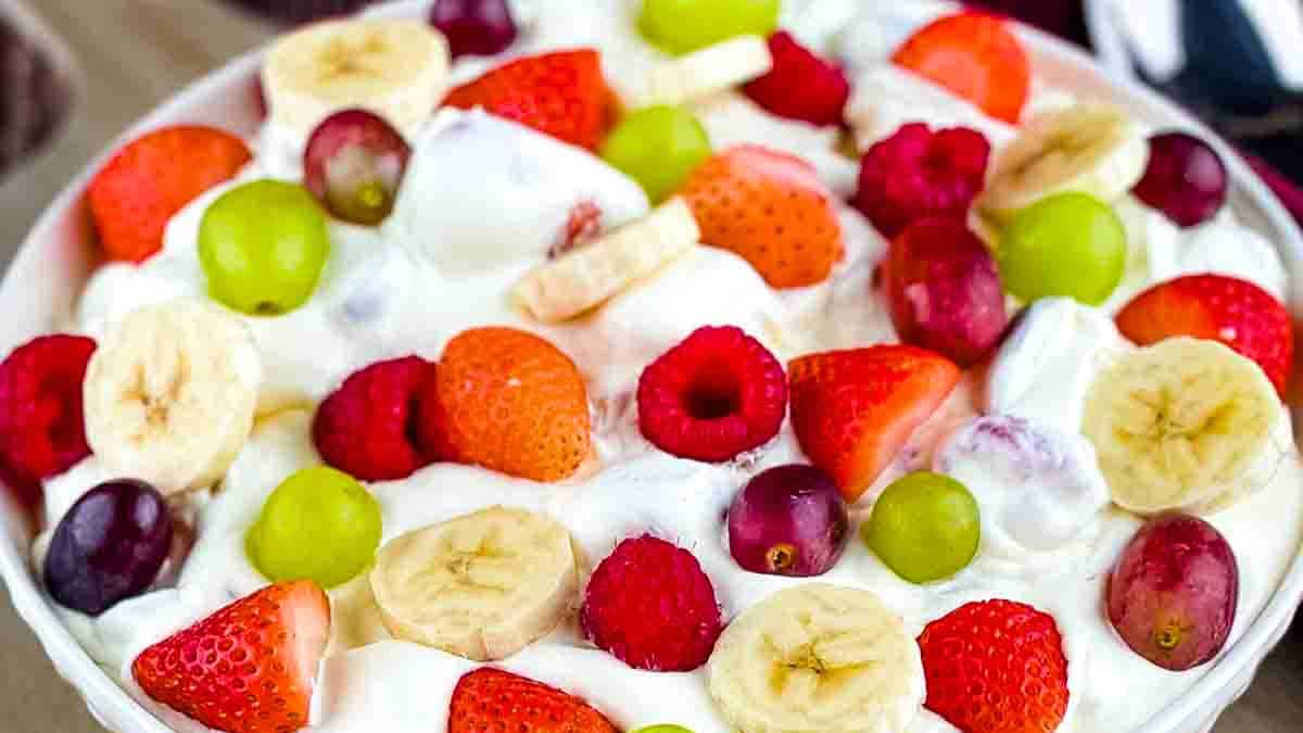 A bowl of fruit salad with Cool Whip and pudding, featuring a vibrant mix of strawberries, blueberries, and pineapple.
