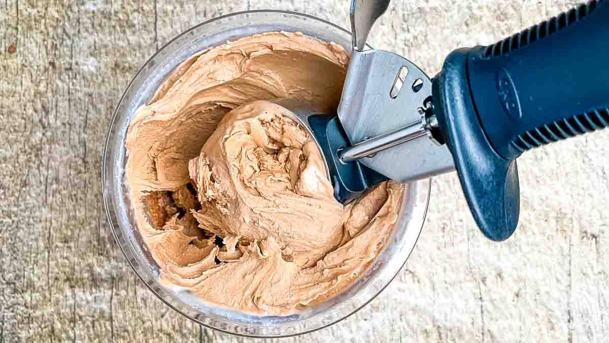 A pint full of homemade Ninja Creami chocolate ice cream about to be scooped up with an ice cream scooper.
