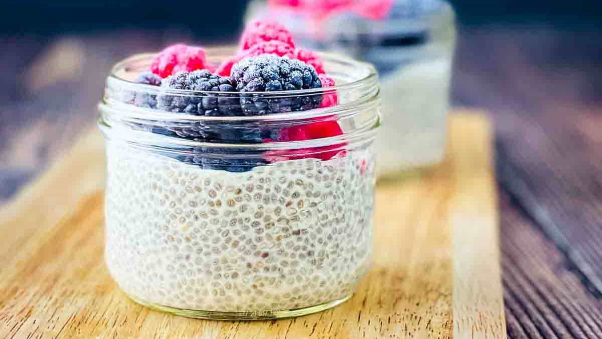 Two small jars filled with oat milk chia pudding, topped with frozen berries.