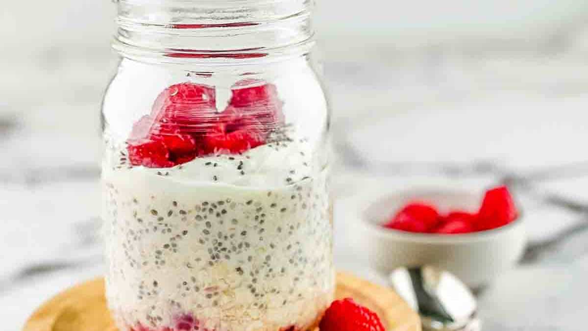 A mason jar filled with raspberry overnight oats, topped with fresh raspberries.