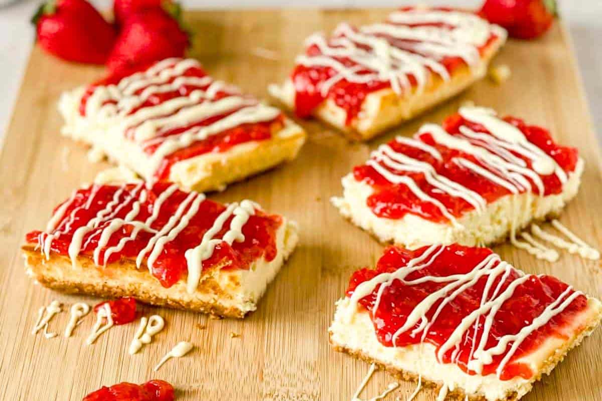A platter of Strawberry Cheesecake Snack Bars, neatly cut into squares, showcasing layers of crumbly crust, rich cheesecake, and a vibrant strawberry topping.
