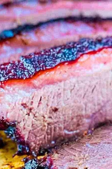 Sliced smoked beef brisket with a dark, flavorful crust, served on a wooden cutting board.