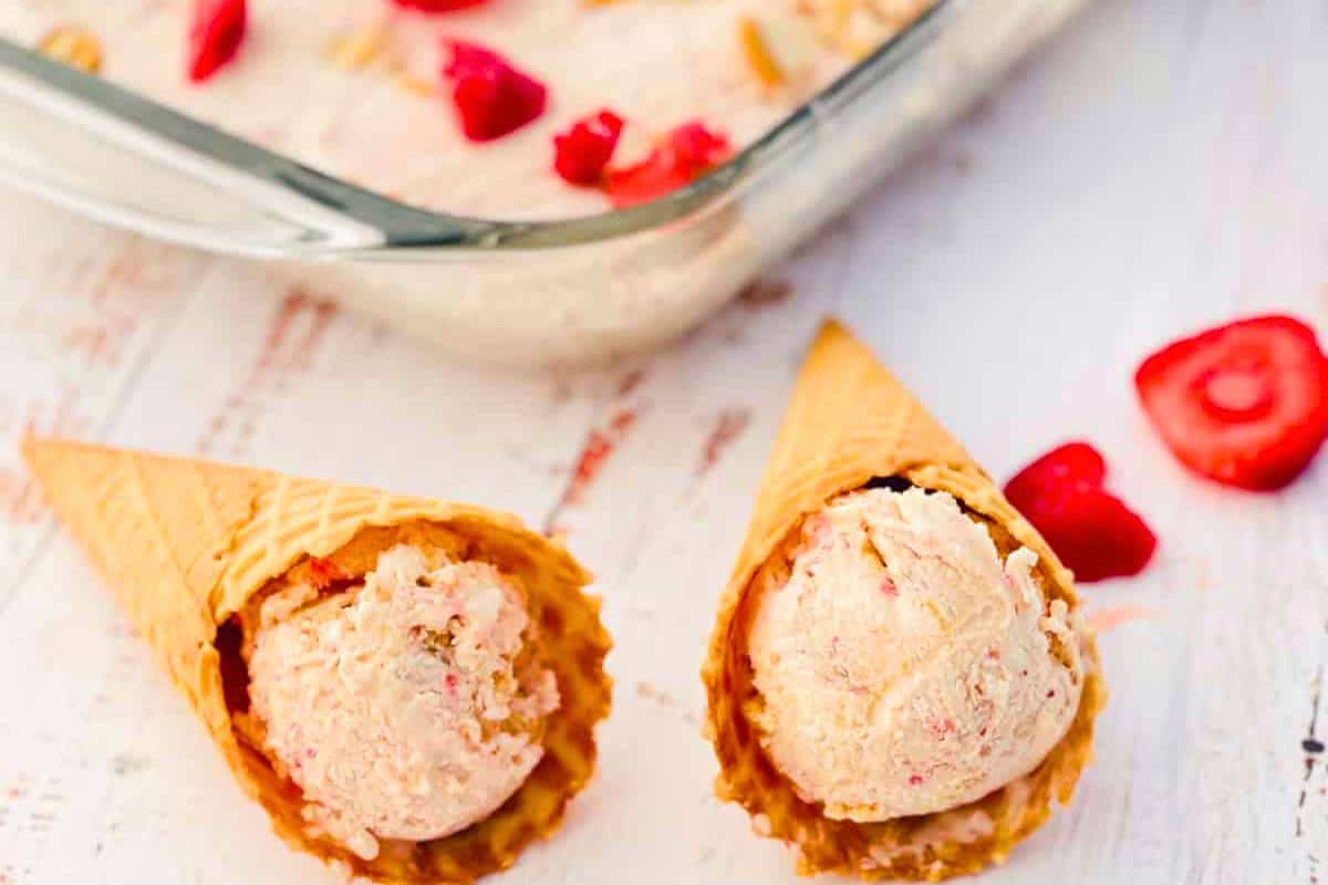 Two waffle cones with freshly made Easy Strawberry Cheesecake Ice Cream, featuring swirls of creamy cheesecake and vibrant strawberry pieces, served chilled for a delightful dessert.