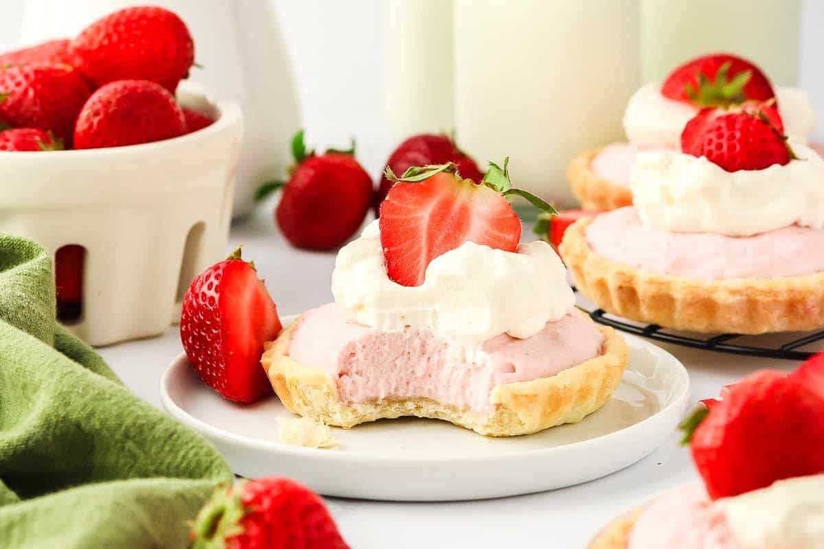 Mini Strawberry Mousse Tartlets, each featuring a flaky crust filled with light strawberry mousse and topped with fresh strawberries, arranged beautifully on a serving tray for a sophisticated Mother's Day treat.