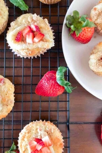 Strawberry rhubarb muffins stuffed with cream cheese filling and garnished with fresh strawberries on a cooling rack.