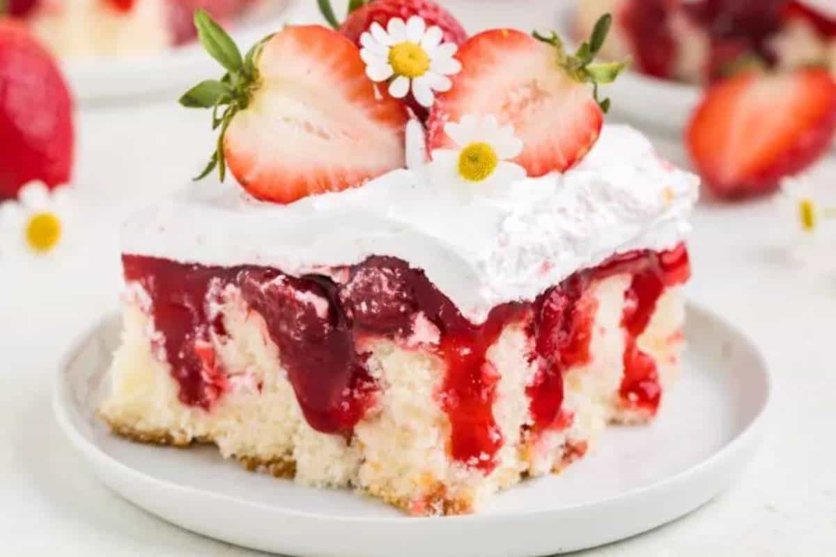 A slice of Strawberry Shortcake Poke Cake on a plate, showcasing layers of fluffy white cake with pockets of sweet strawberry pie filling, topped with a light whipped cream, creating a simple yet appealing treat.