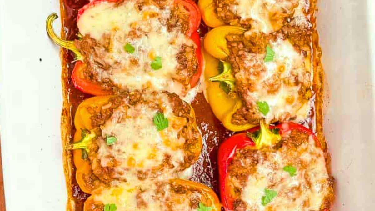 Stuffed bell peppers in a casserole dish, topped with melty cheese and garnished with fresh parsley.