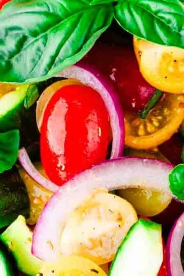 A bowl of Tomato Basil Cucumber Salad featuring sliced tomatoes, cucumbers, and fresh basil, drizzled with a light vinaigrette.