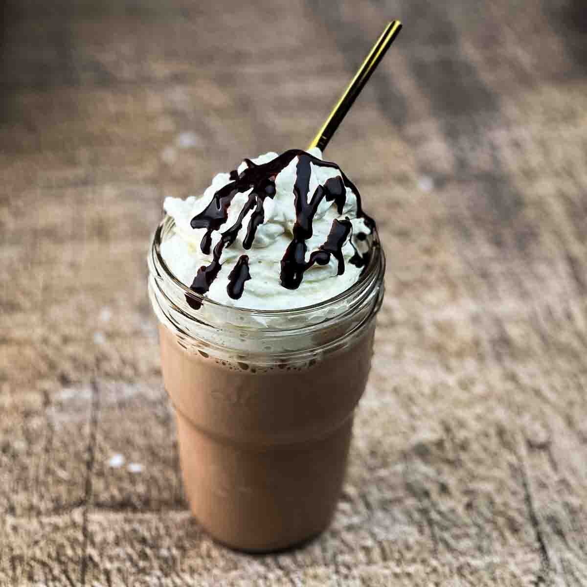A tall chocolate milkshake in a glass topped with whipped cream and chocolate drizzle.