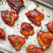 Smoked Huli Huli chicken thighs on a sheet pan, garnished with fresh herbs.