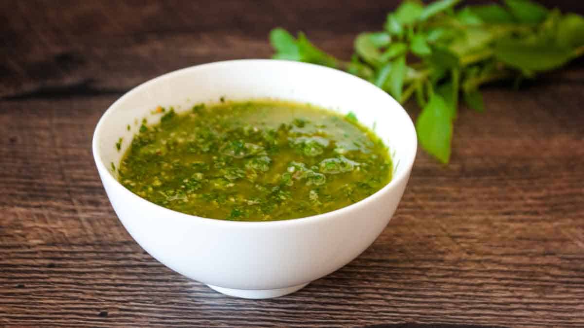 A white serving bowl filled with chimichurri sauce with basil.