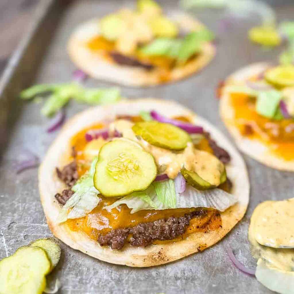 A baking sheet with three Big Mac smash burger tacos with lettuce, pickles, onions, and sauce.