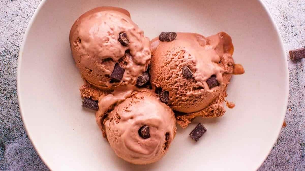 Homemade chocolate ice cream in a white bowl with chunks of dark chocolate sprinkled on top.