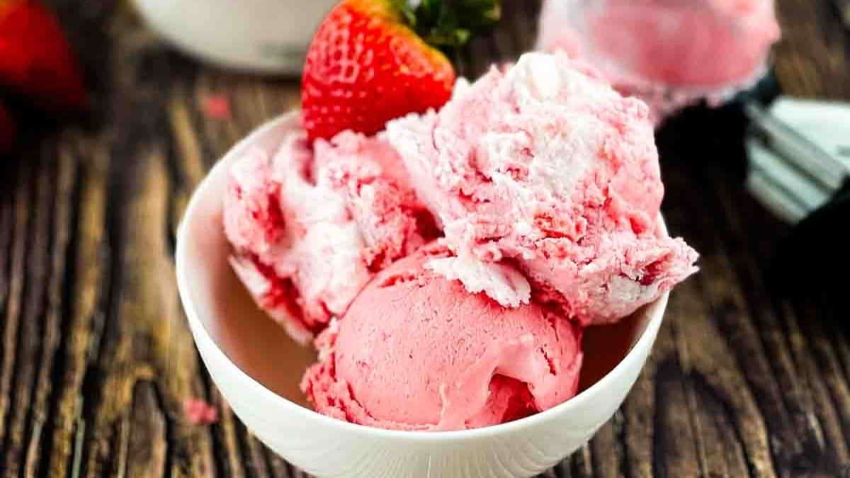 A bowl of strawberry ice cream garnished with a fresh whole strawberry.
