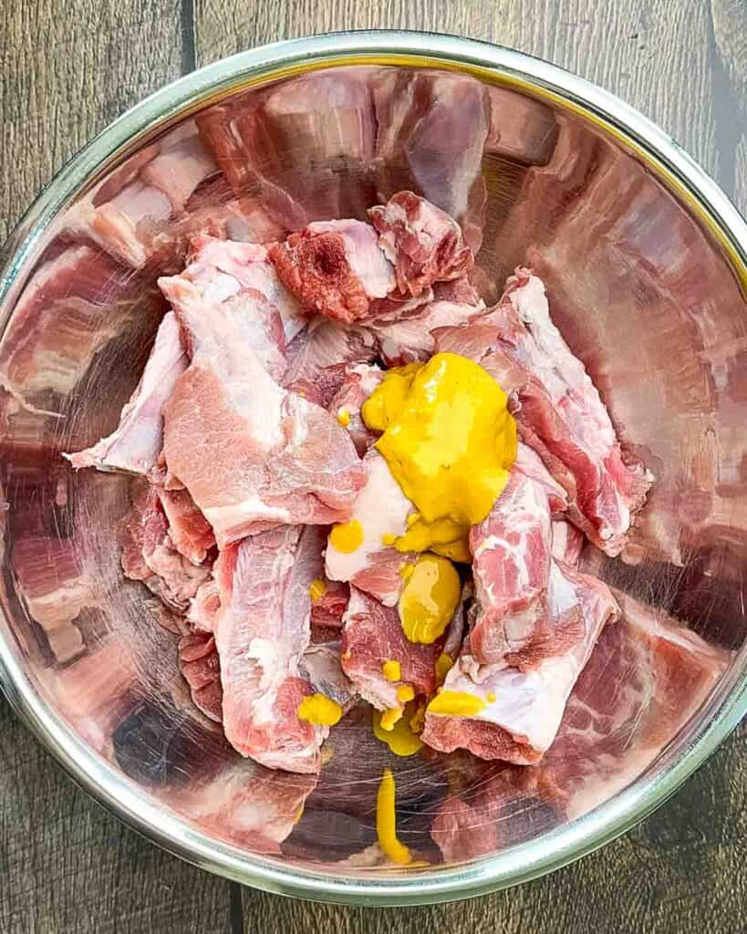 Tossing yellow mustard onto single ribs in a large bowl to help the seasoning stick.
