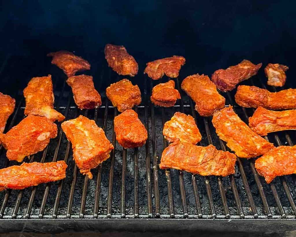 Placing seasoned ribs directly on the smoker grates with smoke rising.