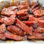 A foil pan of smoked party ribs with a glossy BBQ glaze.
